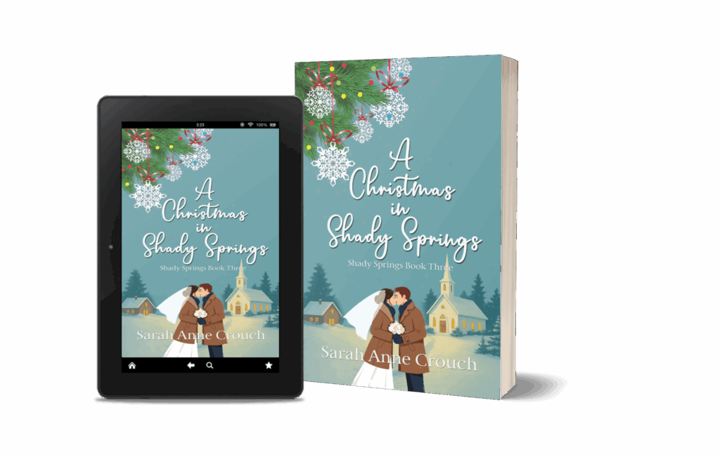 Cover image of A Christmas in Shady Springs by Sarah Anne Crouch, showing a bride and groom sharing a winter kiss in front of a snow-covered church with pine trees and Christmas lights, displayed as both a paperback and eBook.