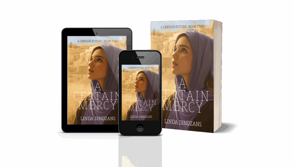 A 3D promotional graphic displaying multiple formats of the book A Certain Mercy by Linda Dindzans, Book Two in the A Certain Future series. The image shows a paperback, a tablet, and a smartphone featuring the same cover art. The cover depicts a young woman in a lavender headscarf gazing upward with a soft, hopeful expression. Behind her is a warm-toned ancient cityscape of stone buildings glowing in golden light.