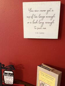 Framed quote by C.S. Lewis about tea and books hanging on a red wall above a shelf with a vintage Alice’s Adventures in Wonderland book and a small “Heather’s Library” sign, creating a cozy literary display.