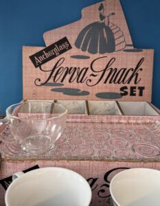 Vintage Anchor Hocking “Sena-Shack” snack set display with a clear glass teacup and textured glass tray, shown in its original pink box with a blue background.