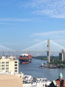 View of the Savannah River in Savannah, Georgia, featuring the Talmadge Memorial Bridge and cargo ships along the historic riverfront on a sunny day.