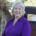 Author Jenny Carlisle smiling outdoors in a purple blouse, standing beside a vintage truck and fall decorations.