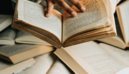Close-up of hands flipping through an open book surrounded by stacked books with text “Big reading life, small budget,” symbolizing reading more books affordably.