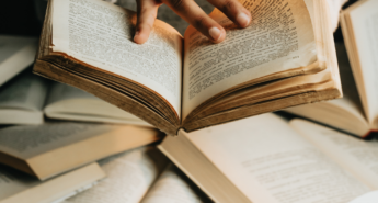 Close-up of hands flipping through an open book surrounded by stacked books with text “Big reading life, small budget,” symbolizing reading more books affordably.
