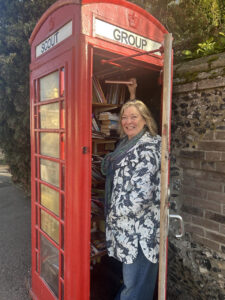 Woman smiling inside a classic red British phone booth repurposed as a small community book exchange.