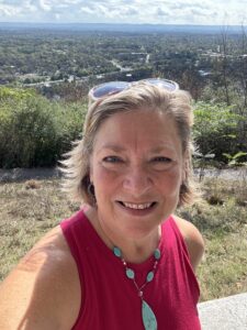 Woman smiling in a selfie at a scenic overlook with a wide landscape view in the background.
